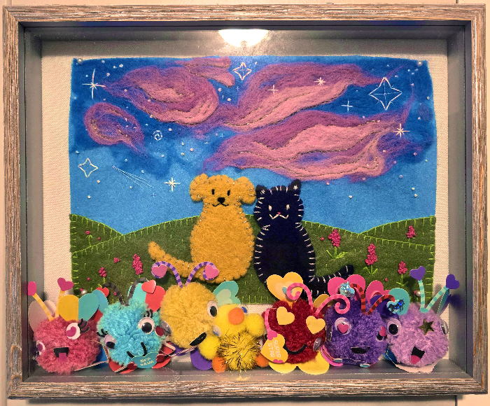 a shadowbox full of fluffy pom pom critters, including a duck, and a felted painting of a dog and a cat watching a sunset;